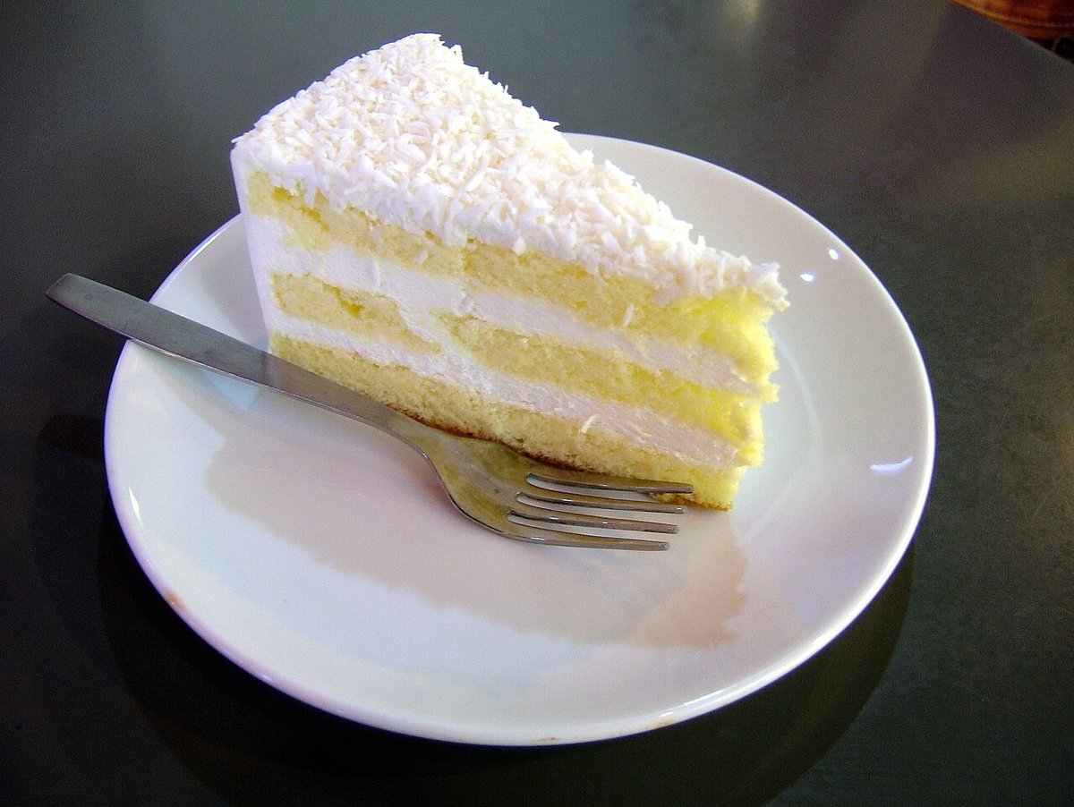 Fatia de bolo branco em camadas com creme e coco ralado por cima