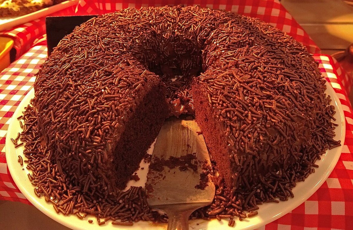 Bolo de brigadeiro coberto de chocolate granulado com uma fatia cortada