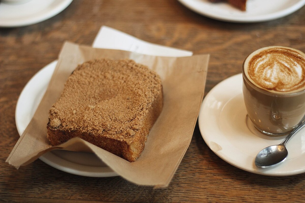 Fatia de bolo com farofa doce por cima servida ao lado de um café