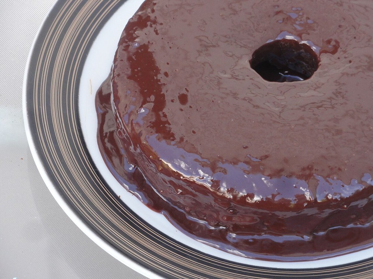 Bolo de chocolate redondo coberto com ganache brilhante escorrendo no prato