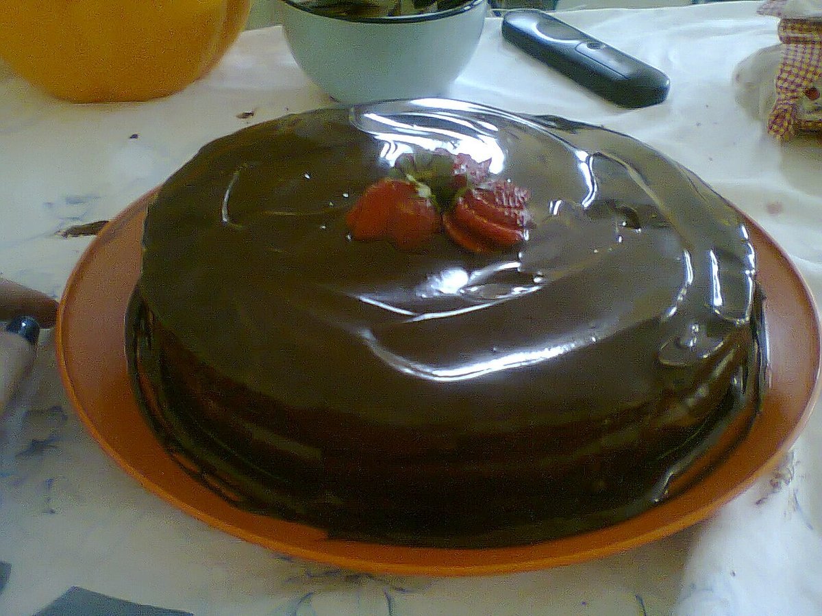 Bolo de chocolate inteiro coberto com calda brilhante e morangos no topo