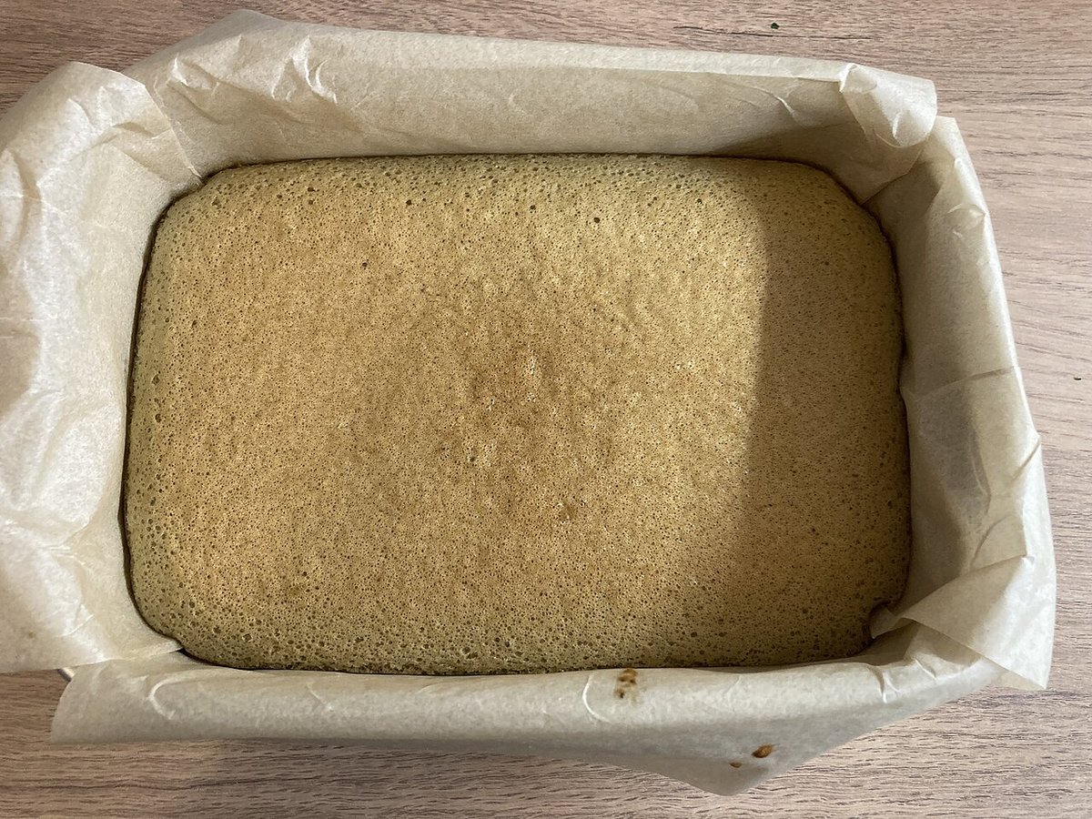 Bolo simples dourado recém-assado em forma retangular forrada com papel-manteiga